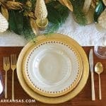 Gold tableware and greenery centerpiece on wooden table.