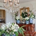 Gold chandelier with candles and floral arrangements in a dining room.