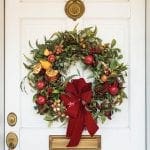 White door with a large wreath of greenery, fruit, and a red bow.
