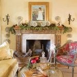 Gold-framed painting above a mantelpiece decorated with pinecones and plates.