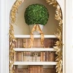 White arched shelf with gold foliage and books, featuring a topiary.