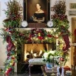 Decorated fireplace mantel with garland, wreath, and artwork.