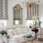 White sofa with patterned drapes, ornate mirror, and chandelier.