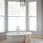 Gray bathroom with a freestanding tub, window, and lantern.