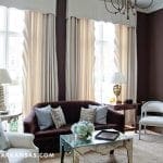 Dark brown walls with beige curtains and a velvet sofa.