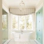 White bathtub in a luxurious bathroom with patterned drapes and a large window.