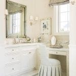 White vanity with marble countertop, mirror, and upholstered chair.