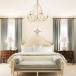 Cream bedroom with a large chandelier, curtains, and a bed.