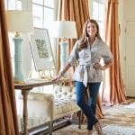 Woman stands before a console table with artwork and lamps.