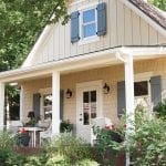 Yellow house with gray shutters and a covered porch with white furniture.