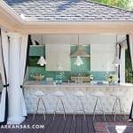 Outdoor kitchen with white cabinets, teal backsplash, and tufted bar front with white stools.
