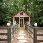 Wooden chicken coop with a stone path and decorative chickens in a wooded setting
