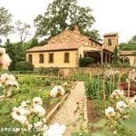 Stone and stucco house with tile roof, surrounded by gardens and trees.