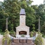 Stone fireplace with metal hood, outdoor sofa, and decorative planters