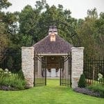 Stone gateposts and black metal fence opening to a covered pavilion with outdoor seating.