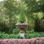 Ornate urn planter with evergreen topiary and pink flowers in garden