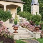 Stone steps leading to arched entryway, flanked by pink flowers and urns.