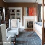 Bedroom with brown walls, four-poster bed, fireplace, and armchair with ottoman.