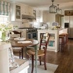 Cream kitchen with stainless steel appliances, island, and dining nook with striped roman shades.