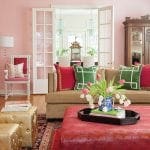 Living room with pink walls, tan sofa, red ottoman, and gold ottomans.