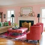 Living room with pink walls, tan sofa, red ottoman, and ornate fireplace.
