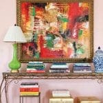 Abstract painting above console table with books, green lamp, and blue ginger jar