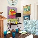 Dining room with abstract fruit painting, blue chandelier, and patterned chairs.