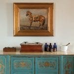 Turquoise cabinet with gold detailing, topped with antique scales, bottles, and mortar and pestle.