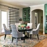 Dining room with round table, patterned chairs, green cabinetry, and striped curtains.