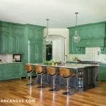 Green kitchen with island, wood stools, and pendant lights