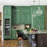 Green kitchen cabinets with wine fridge, granite island, and bar stools