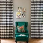 Green leather armchair with patterned pillow and ottoman, flanked by striped curtains.