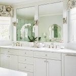 White double vanity with marble countertop, brass fixtures, and mirrors.