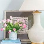 White lamp, vase of pink tulips, and books on a dark wood surface.