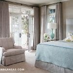 Bedroom with light blue bed, floral pillow, armchair, and French doors to balcony.