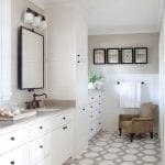 White bathroom with marble countertop, custom cabinetry, and geometric floor tiles.
