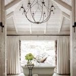 White bathroom with freestanding tub, stone wall, and vaulted wood ceiling