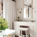 White bathroom with clawfoot tub, stone accent wall, marble vanity, and stool.
