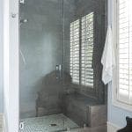 Glass shower with gray tile walls, white mosaic tile floor, and built-in bench.