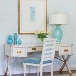 White desk with blue velvet chair, blue vases, and framed art