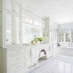 White bathroom with double vanity, hexagonal marble floor, and soaking tub.