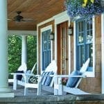 Porch with white Adirondack chairs, blue windows, wood siding, and hanging flowers.