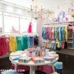 Clothing boutique interior with racks of colorful dresses and t-shirts, round display table.