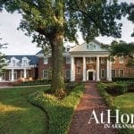 Brick mansion with white columns and balconies, surrounded by trees and manicured lawns.