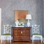 Hallway with blue textured wallpaper, antique dresser, two white chairs with green seats, and