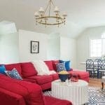 Red sectional sofa with blue and white pillows, white shag throw, and popcorn on coffee table.
