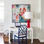 White desk with laptop, blue bamboo chair, and abstract floral art.