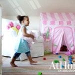 Girl holding stuffed animal in playroom with pink play tent and crib