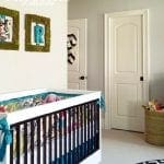 Nursery with white crib, colorful bedding, moss-framed art, and two white doors.