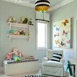 Nursery with white storage bench, plush toys, butterfly art, and striped rug.